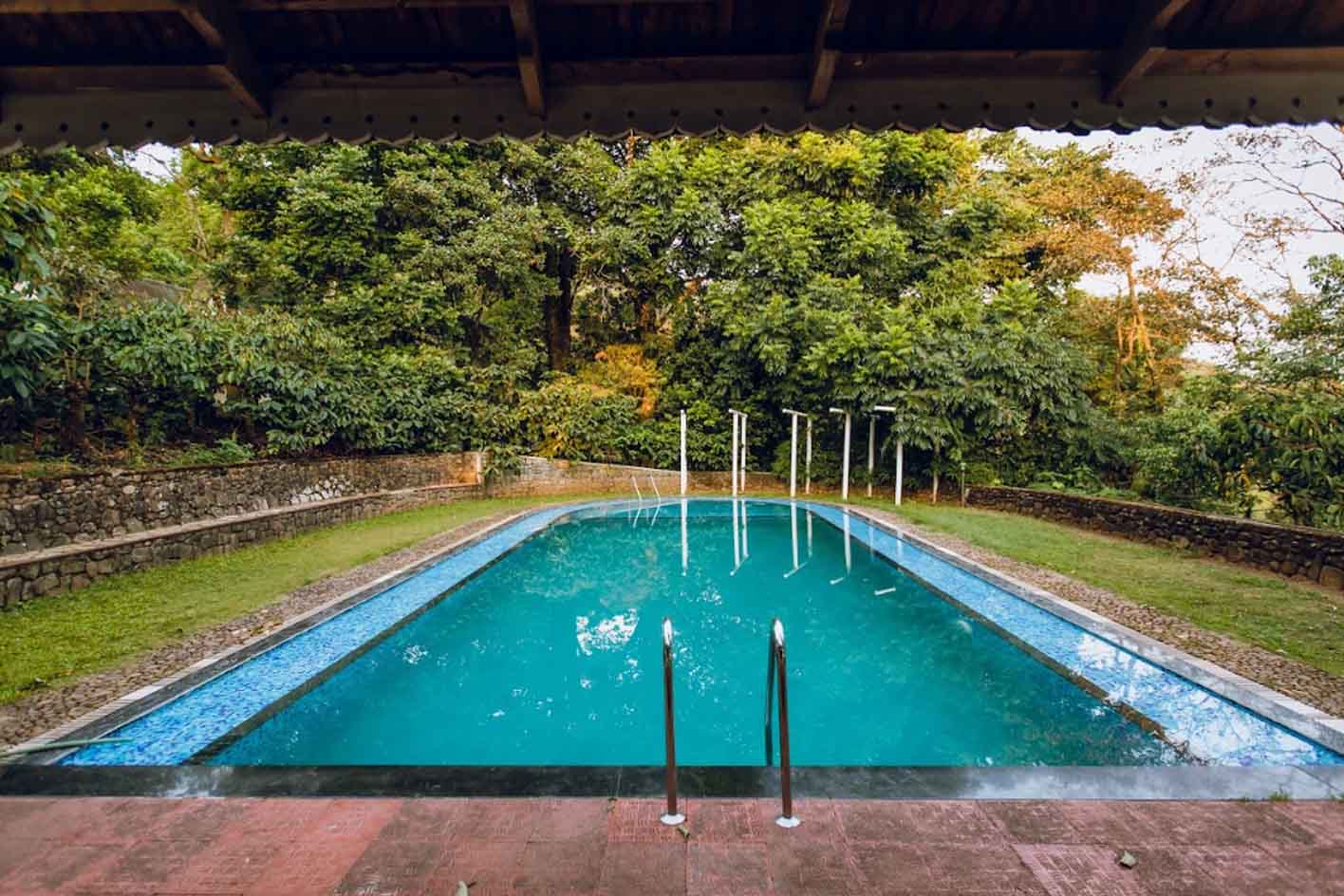 Open-air swimming pool surrounded by lush greenery at Misty Woods Resort Coorg