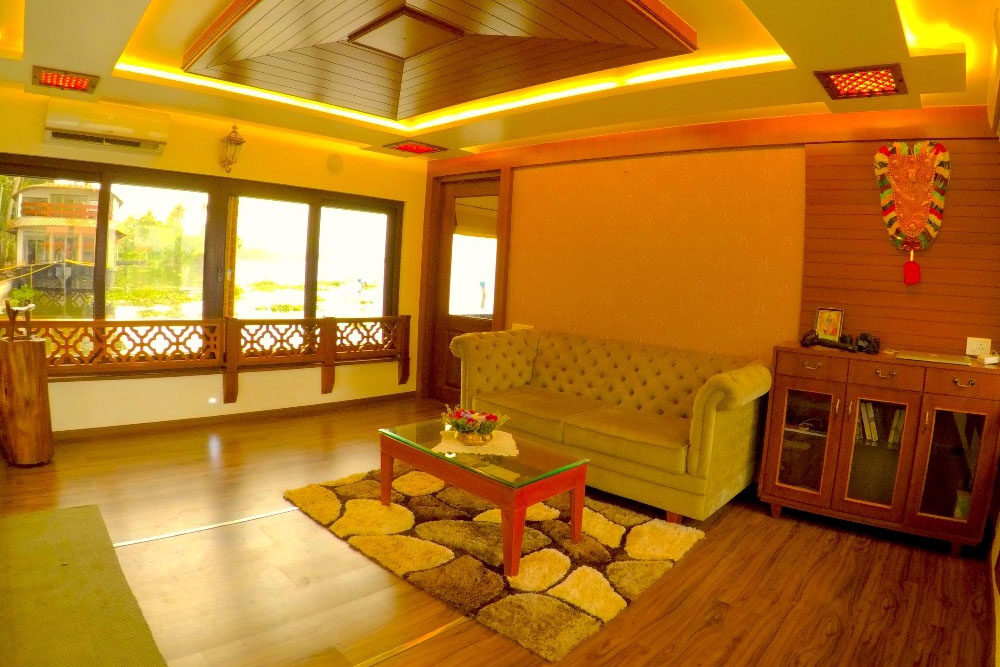 Spacious living area of a 1 bedroom ultra luxury houseboat in Alleppey with a sofa, wooden ceiling and backwater-view windows